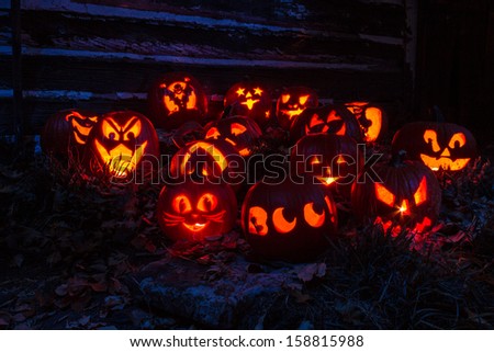 Carved Halloween pumpkins lit with candles sitting on leaves in front of old barn lit with purple light