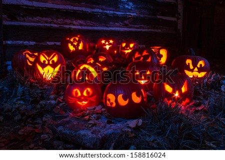 Carved Halloween pumpkins lit with candles sitting in front of old barn lit with purple light
