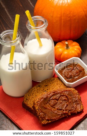 Heart shape drawn in pumpkin butter on slices of pumpkin bread sitting on orange napkin with 2 glasses of milk with yellow straws