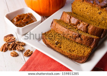 White plate with pumpkin bread and pecan nuts and container of pumpkin butter