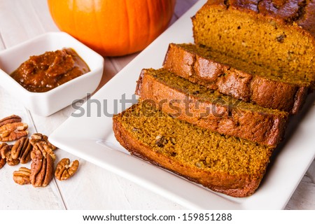 Loaf of pumpkin bread sitting on white plate and container filled with pumpkin butter and pecan nuts