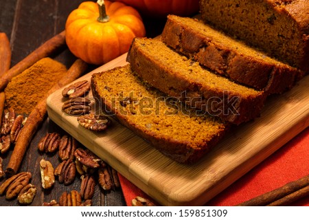 Sliced loaf of pecan cinnamon pumpkin bread sitting on wooden cutting board with orange napkin