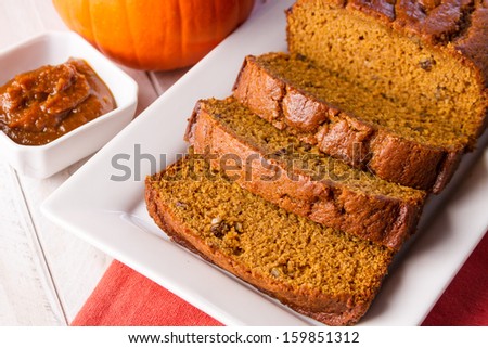 Loaf of pumpkin bread sitting on white plate with orange napkin and container filled with pumpkin butter