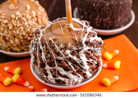 Chocolate and pecan covered hand dipped caramel apples sitting on orange napkin with candy corn
