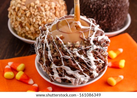 Pecan and chocolate covered caramel apple sitting on orange napkin with candy corn