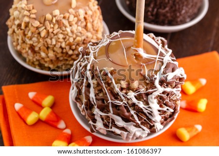 Homemade caramel apples sitting on orange napkin with candy corn on wooden table