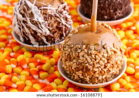 Close up of hand dipped caramel apple decorated with peanuts sitting on candy corn