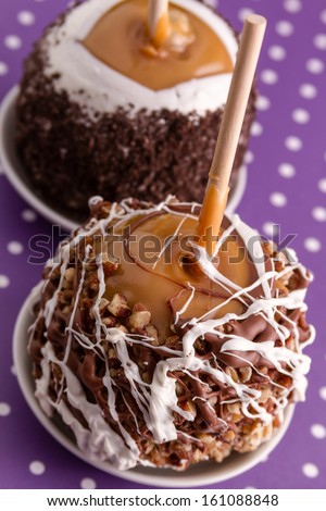 Hand dipped caramel apples covered with pecans and chocolate on purple polka dot background