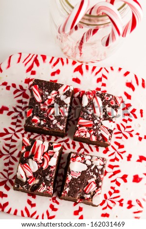 Display of homemade peppermint fudge sitting on melted candy plate with jar of candy canes
