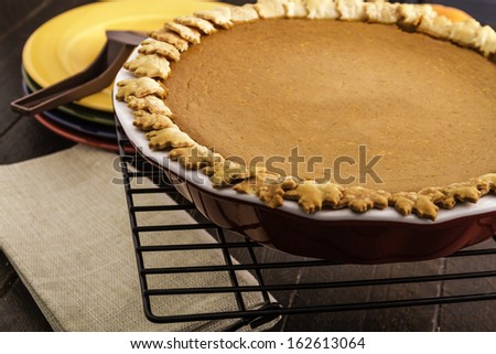 Home baked pumpkin pie sitting on wire baking rack with stack of colorful plates