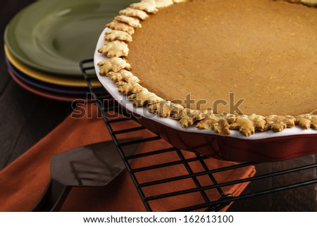 Close up of pumpkin pie sitting on wire baking rack with stack of colorful plates