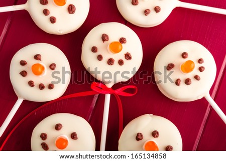 Display of homemade holiday snowmen cookie pops sitting on red wooden table