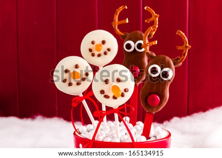 Homemade reindeer and snowmen cookie pops on sticks against red background