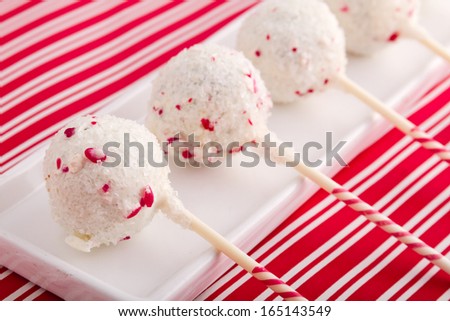 Row of peppermint brownie cake pops on white plate sitting on red striped background