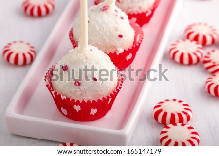 Row of peppermint brownie cake pops standing in red polka dot cups on white plate and peppermint candies