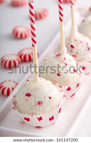 Row of peppermint brownie cake pops standing in red and white polka dot cups on white plate and peppermint candies with red ribbon