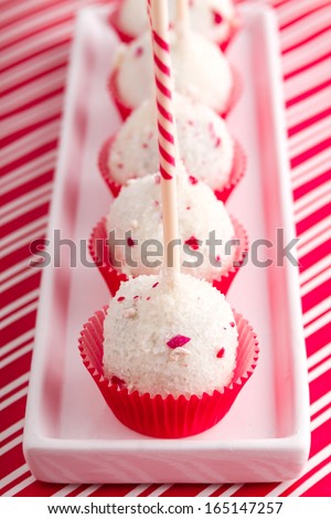 Row of peppermint brownie cake pops standing in red cups on white plate and red striped background