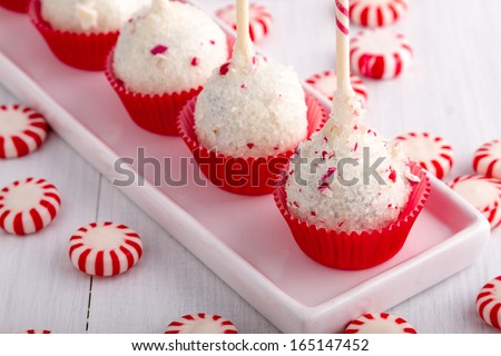 Row of peppermint brownie cake pops standing in red cups on white plate and peppermint candies