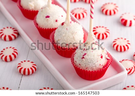 Row of peppermint brownie cake pops standing in red cups on white plate and peppermint candies