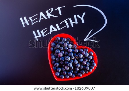 Fresh organic blueberries in red heart shaped bowl with white chalk writing on black chalkboard