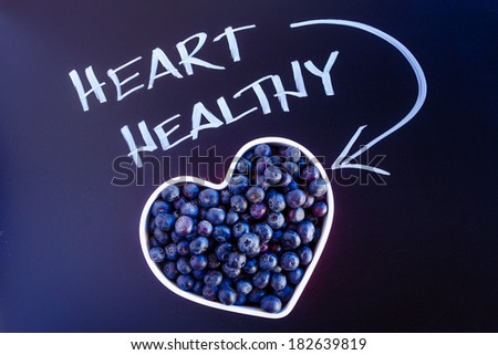 Fresh organic blueberries in white heart shaped bowl with white chalk writing on black chalkboard