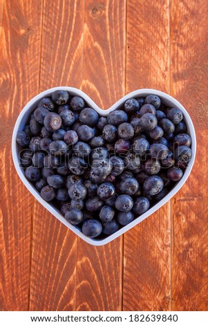 Fresh organic blueberries in white heart shaped bowl on wooden table