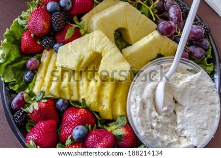 Assorted fruit tray with strawberries, blueberries, grapes, pineapple, blackberries and cheese dip sitting on table