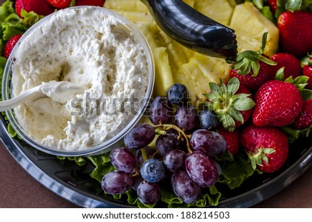 Assorted fruit tray with strawberries, blueberries, grapes, pineapple, blackberries and cheese dip sitting on table