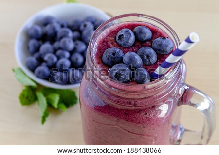 Mason jar filled with blueberry and blackberry fresh fruit smoothie sitting on counter with bowl of blueberries