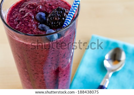 Glass filled with blueberry and blackberry fresh fruit smoothie sitting on counter with light blue napkin and spoon