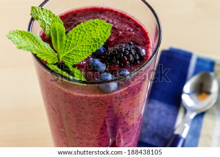 Close up of glass filled with blueberry and blackberry fresh fruit smoothie sitting on counter with blue checked napkin and spoon