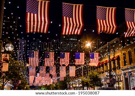 Display of American flags hanging above street with twinkling lights