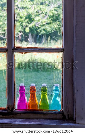 Looking through old window at colored vintage bottles sitting on wooden window sill