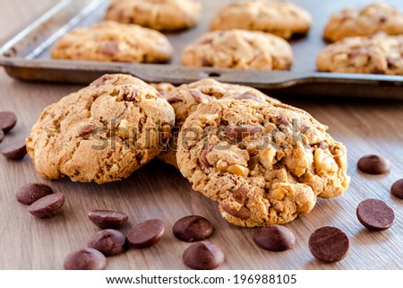Pile of homemade chocolate chip cookies sitting in front of baking pan filled with cookies