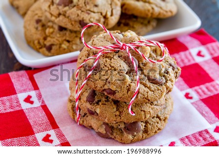 Close up of stack chocolate chip cookies tied with red bakers twine and a plate of cookies sitting on heart napkin