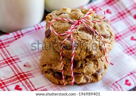 Close up of stack chocolate chip cookies tied with red bakers twine and a plate of cookies sitting on heart napkin