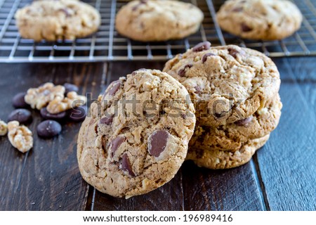 Warm chocolate chip cookies sitting on cooling with stack of cookies in front