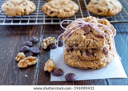 Warm chocolate chip cookies sitting on cooling with stack of cookies in front tied with pink bakers twine