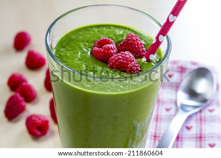 Healthy green fresh fruit and vegetable juice smoothie with red heart straw and raspberry garnish