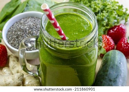 Healthy green juice smoothie surrounded by whole fruits, vegetables and chia seeds with red polka dot straw