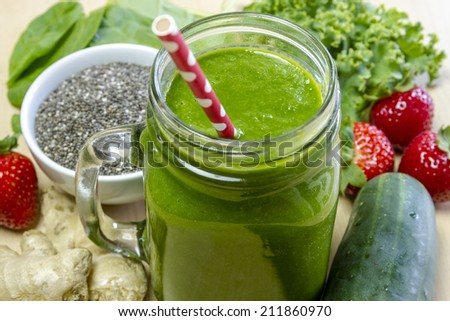 Healthy green juice smoothie surrounded by whole fruits, vegetables and chia seeds with red polka dot straw
