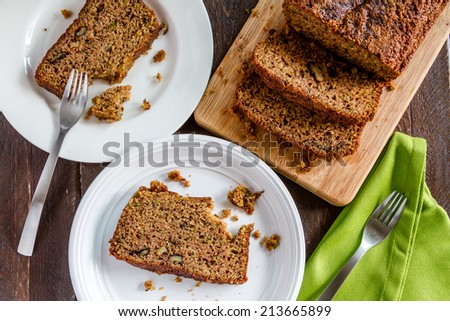 Fresh baked zucchini bread sitting on cutting board and white plates with green napkin and forks