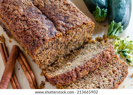 Loaf of homemade zucchini bread sitting on counter with fresh zucchini squash, shreds and cinnamon sticks