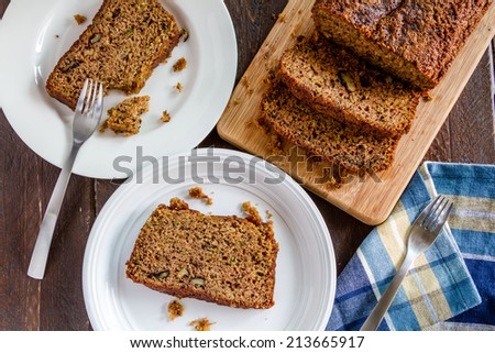 Fresh baked zucchini bread sitting on cutting board and white plates with blue striped napkin and forks