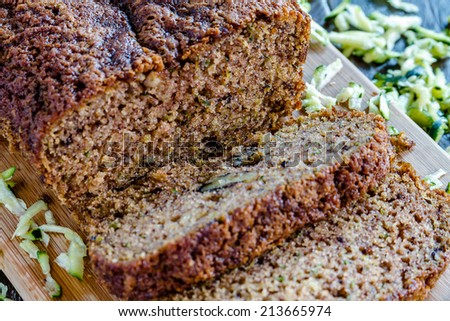 Close up of loaf of homemade zucchini bread sitting on wooden cutting board with fresh shredded zucchini