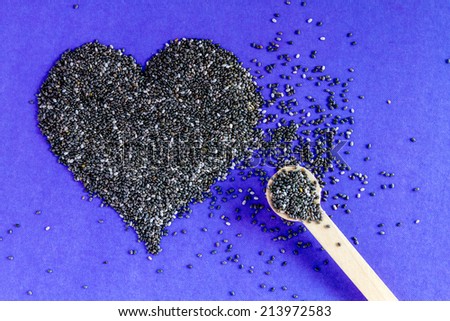 Black chia seeds arranged in heart shape with small spoon on purple background
