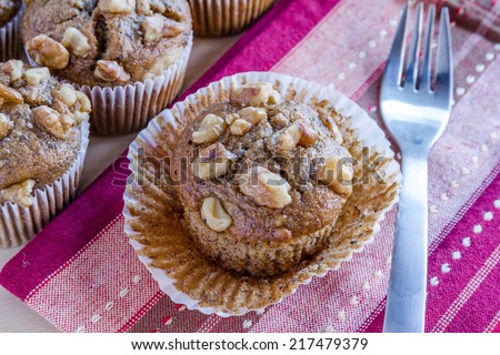 Close up of homemade banana walnut and chia seed muffin with paper removed sitting on red and brown striped napkin with fork