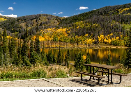Picnic area on shore of mountain lake on warm fall afternoon with brightly colored trees changing color reflecting on water surface