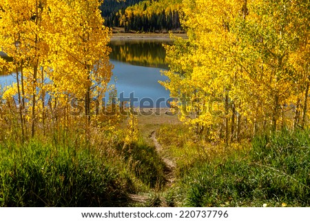 Dirt hiking trail leading to lake and mountain slopes with changing yellow Aspen trees in distance