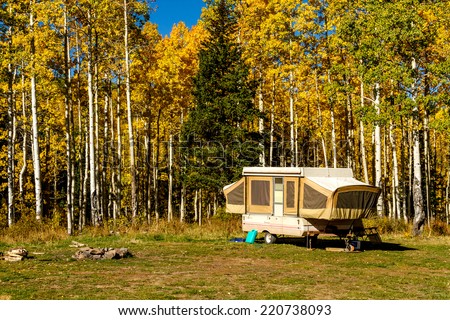 Pop up camper trailer parked in campsite in changing yellow Aspen tree forest on sunny fall morning